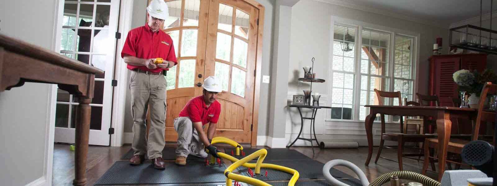 image shows 2 men using tools to dry out flooded floor in a home